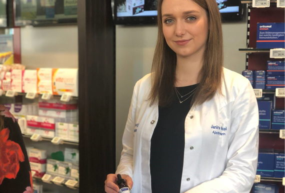 Apothekerin der Arnsburg Apotheke steht hinterm Tresen und hält ein Medikament in der Hand